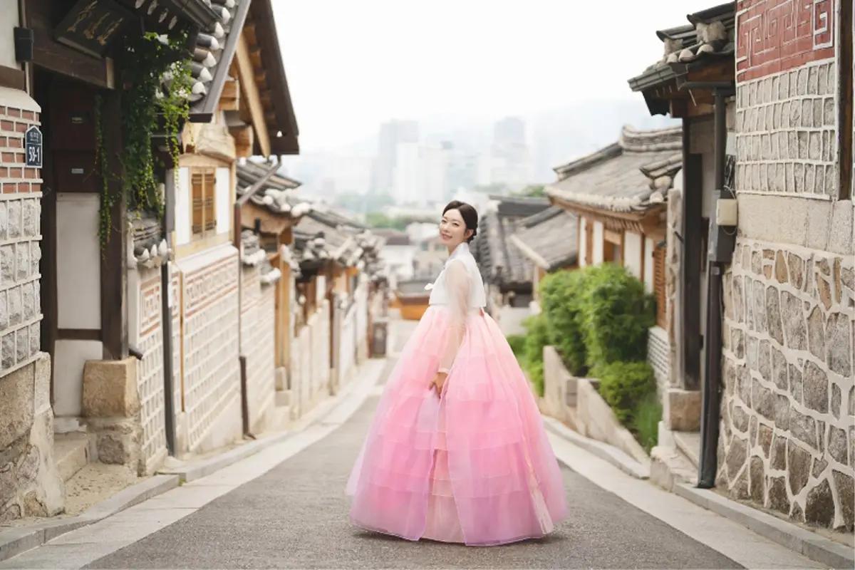 Person wearing pink hanbok walking down a picturesque street in Bukchon Hanok Village.