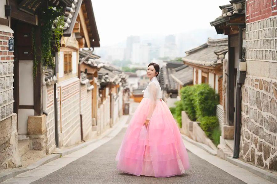 穿著粉紅色韓服站在韓屋村小巷的女子