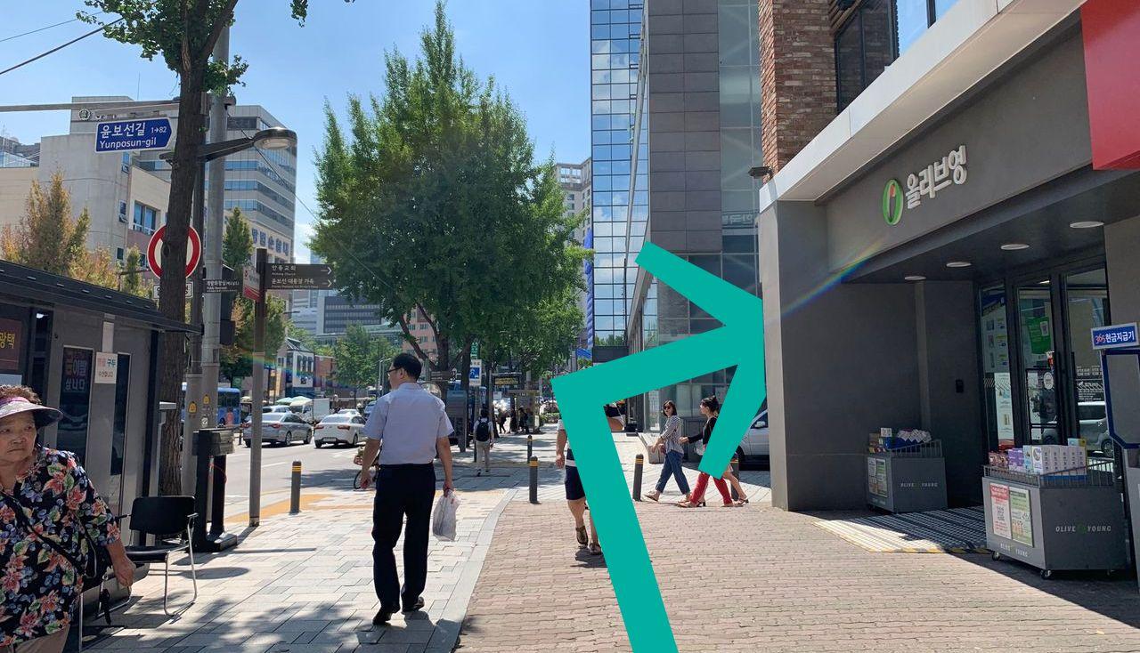 Street view near Olive Young store showing people walking on a sunny day with street signs visible.