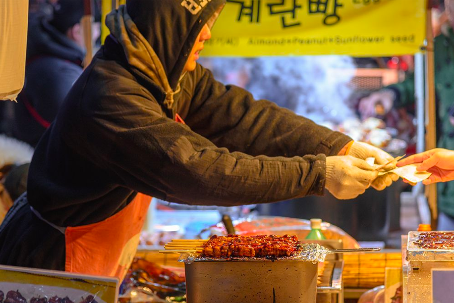 韓國夜市的小吃攤上，攤主忙碌地準備著當季秋冬限定小吃，吸引饕客前來品嚐各種美味。