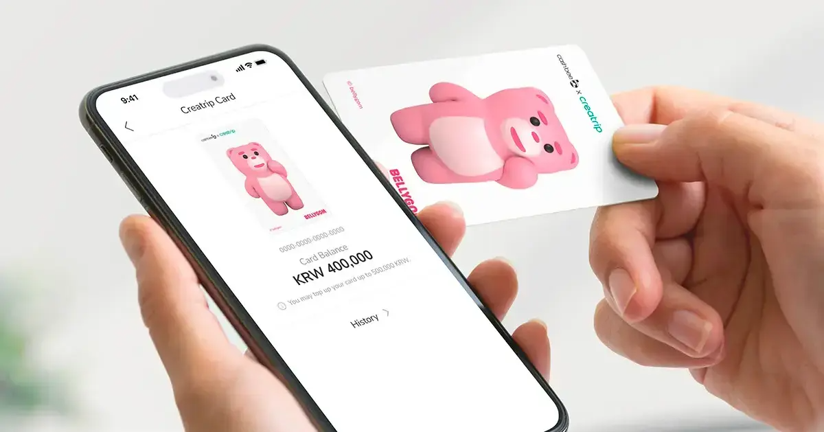 在手機上顯示的Creatrip交通卡“BELLGOM卡”屏幕以及一隻手拿著的Creaptrip粉紅色角色卡片。