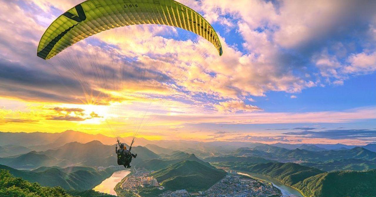 ภาพกิจกรรมพาราไกลดิ้งที่ดันยางในช่วงพระอาทิตย์ตกดินที่งดงามในปลายฤดูร้อน จุดชมวิวทิวทัศน์เหนือภูเขาและแม่น้ำที่กว้างใหญ่น่าทึ่งในเกาหลีใต้