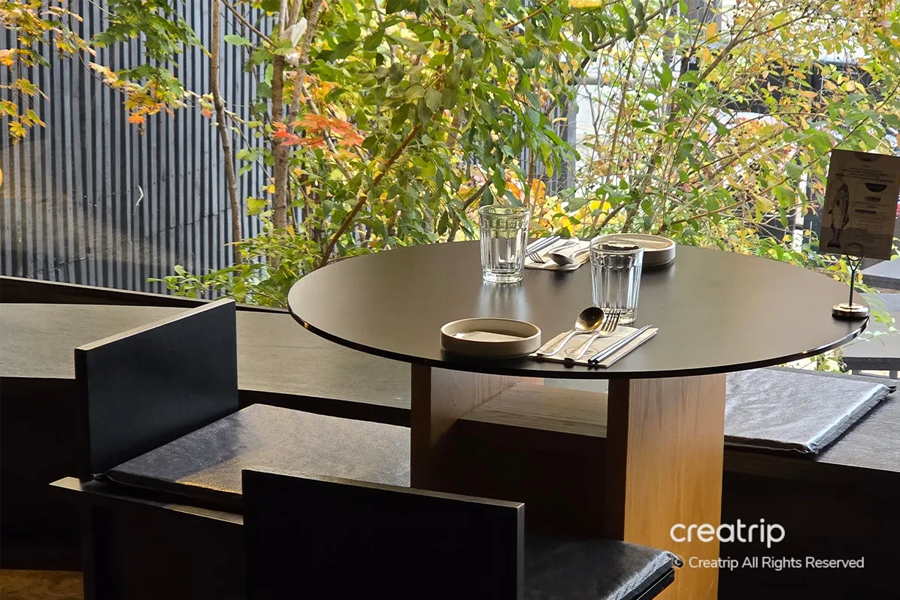 景色優美的餐桌擺放於風景如畫的窗邊，在此享用美食的同時，也能在JINJAK KAKII餐館體驗和諧的自然風情。