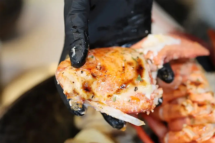 近距離拍攝一隻由海天漁夫餐廳員工拿著的活龍蝦鉗節，揭示了龍蝦肉的嫩滑和醬料的均勻分佈。