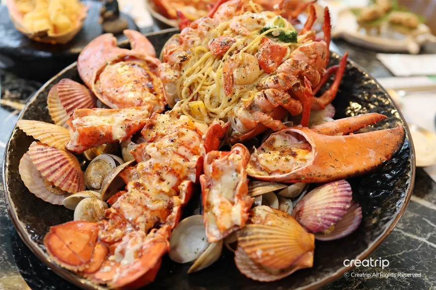 美味可口的海鮮拼盤，中心是用新鮮龍蝦搭配義大利麵組成的主菜，一旁有新鮮的貝類和貝類，完美呈現出海鮮的豐盛與滋味。