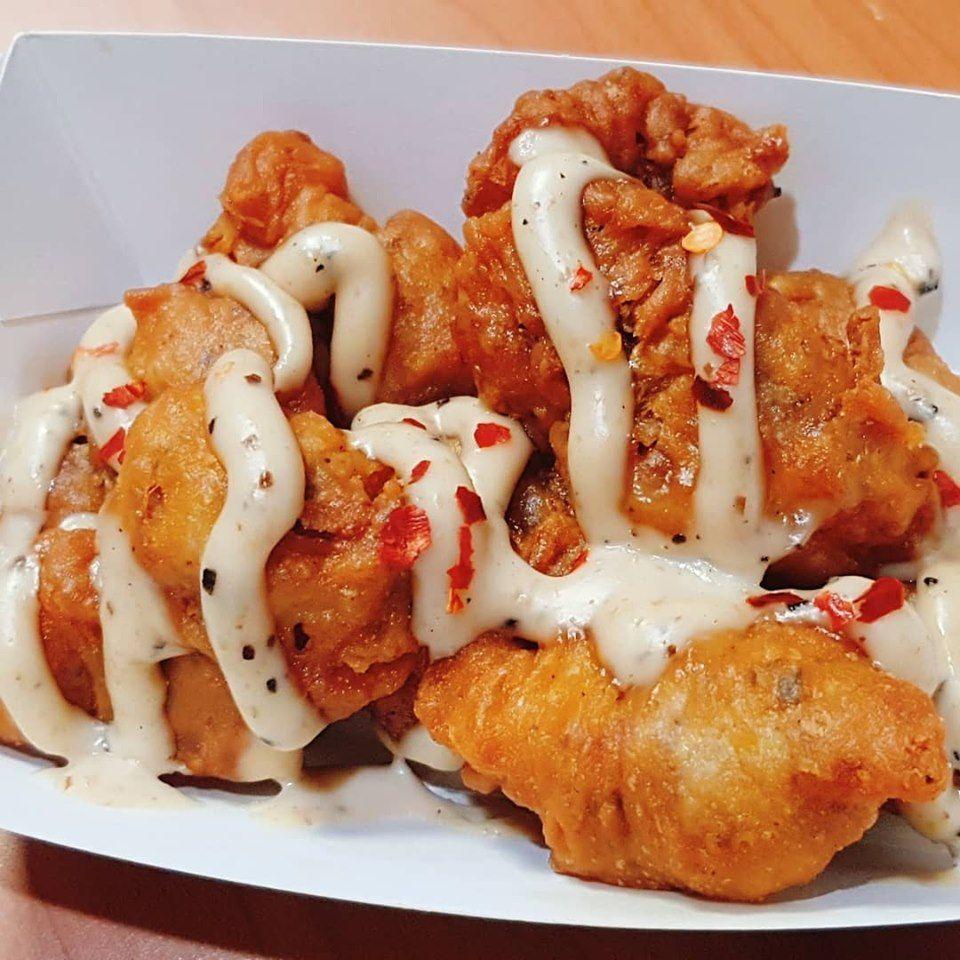 Mollejas de pollo KFC con aderezo y hojuelas de pimiento en un contenedor, capturadas de cerca para apreciar el detalle de su textura crujiente.