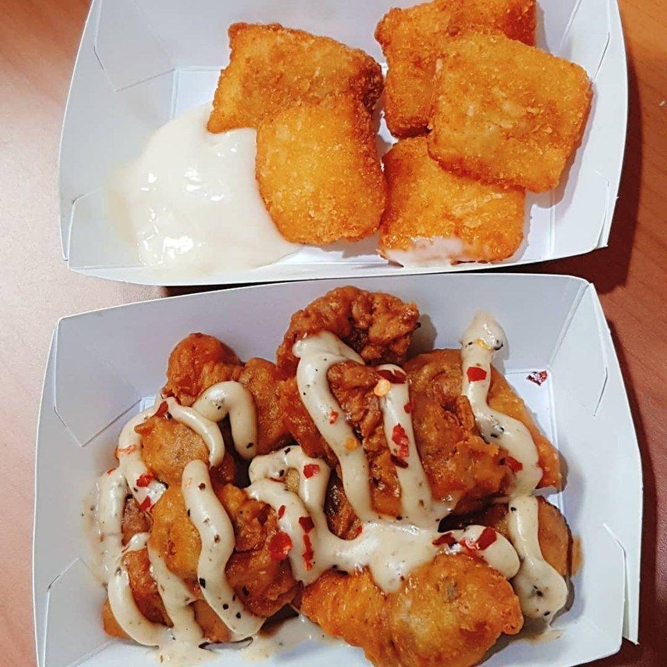 Dos bandejas de comida de KFC, una con mollejas de pollo cubiertas con aderezo y otra con masa frita, acompañadas de un aderezo.