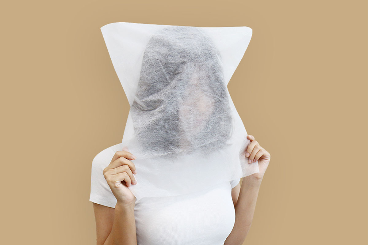 A woman demonstrating the use of a facial cover provided in Korean clothing shops to protect garments during try-ons.