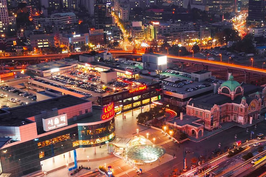韓國首爾車站全景，夜晚亮起的都市燈光，展示繁忙的交通樞紐和鄰近的樂天購物中心。