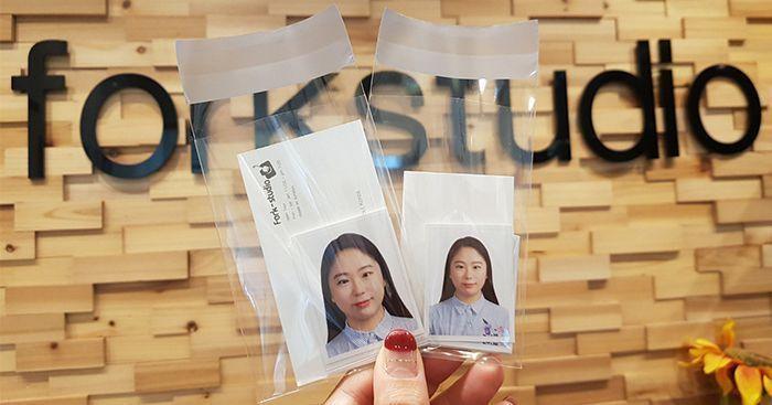 Two ID photo packages held in a hand, with a studio backdrop featuring 'forkstudio' in the background, representing professional ID photo services.