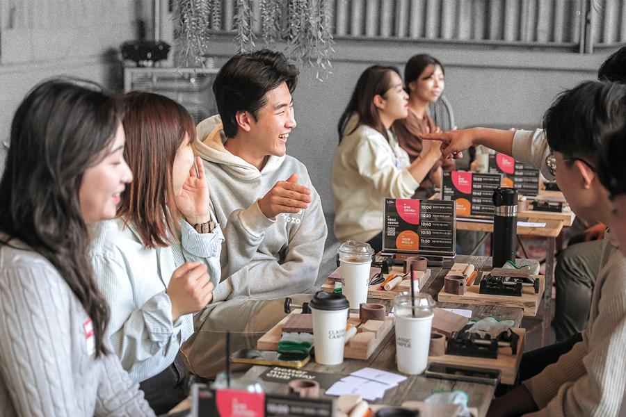 一群年輕人在一間咖啡館似的地方圍坐在桌旁，前面擺放著飲料杯和其他小物品。