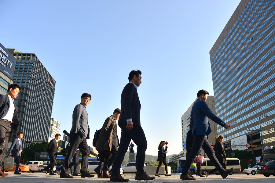 穿著商務西裝的韓國上班族在繁忙的城市街道上行走，高樓大廈背景中顯示出城市的現代化。