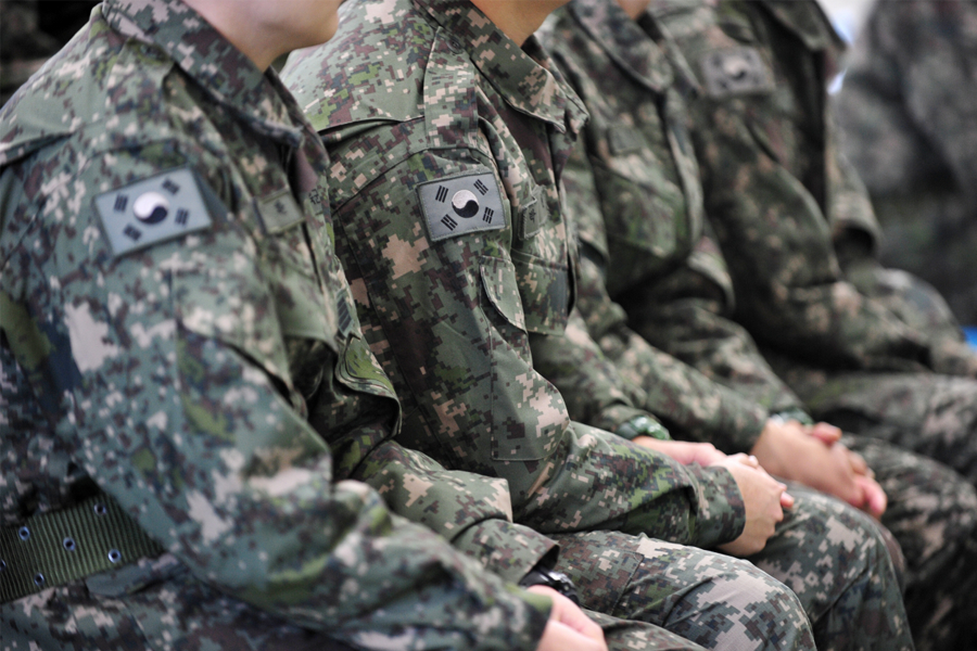 一群韓國軍隊士兵坐成一排，身穿迷彩軍裝，袖子上可以看到韓國國旗的標誌。