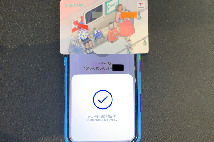 스마트폰 위에 위치한 T-money 카드와 성공적으로 스캔되었다고 표시된 앱 화면.
