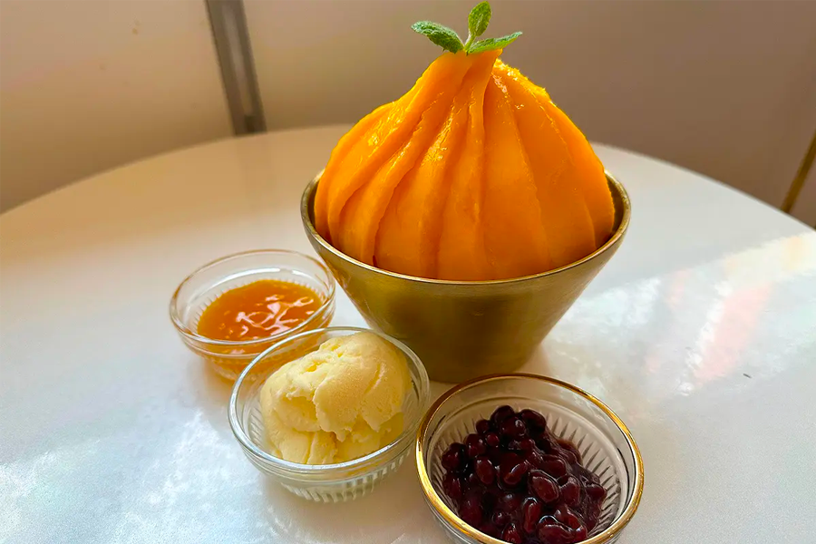 청량한 여름 디저트로 제공되는 리얼 망고 빙수의 모습으로, 다양한 토핑이 함께 있는 모습입니다.