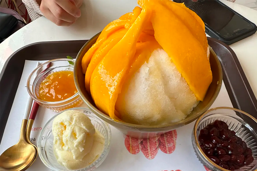 리얼 망고 빙수를 한 숟가락 떠서 먹으려는 모습으로, 망고와 빙수의 조화로운 모습을 보여줍니다.