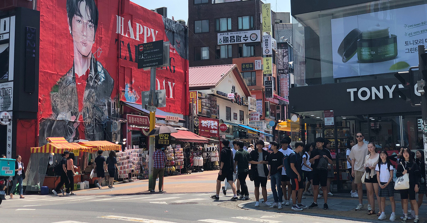 Hongdae street view with vibrant shops, street stalls, and a large billboard, showcasing the lively shopping district in Seoul.