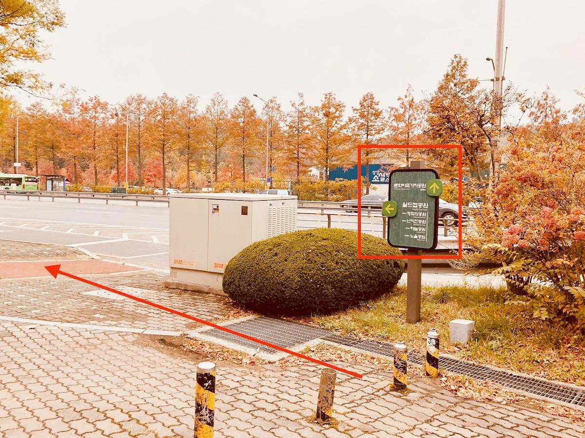 Colored autumn foliage surrounds a directional sign at Oil Tank Culture Park in Mapo, Seoul, indicating the pathway with visible arrows for park visitors.