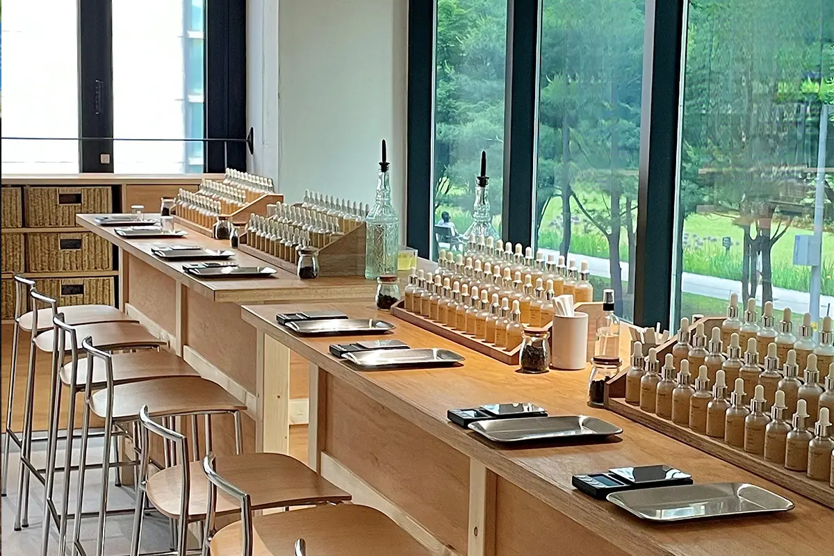 位於弘大的香水DIY工坊,展示用各種香水瓶和調香材料整齊排列在長桌上,旁邊是大窗能眺望外面的綠意盎然的景色,適合進行香水調配的安靜放鬆空間。