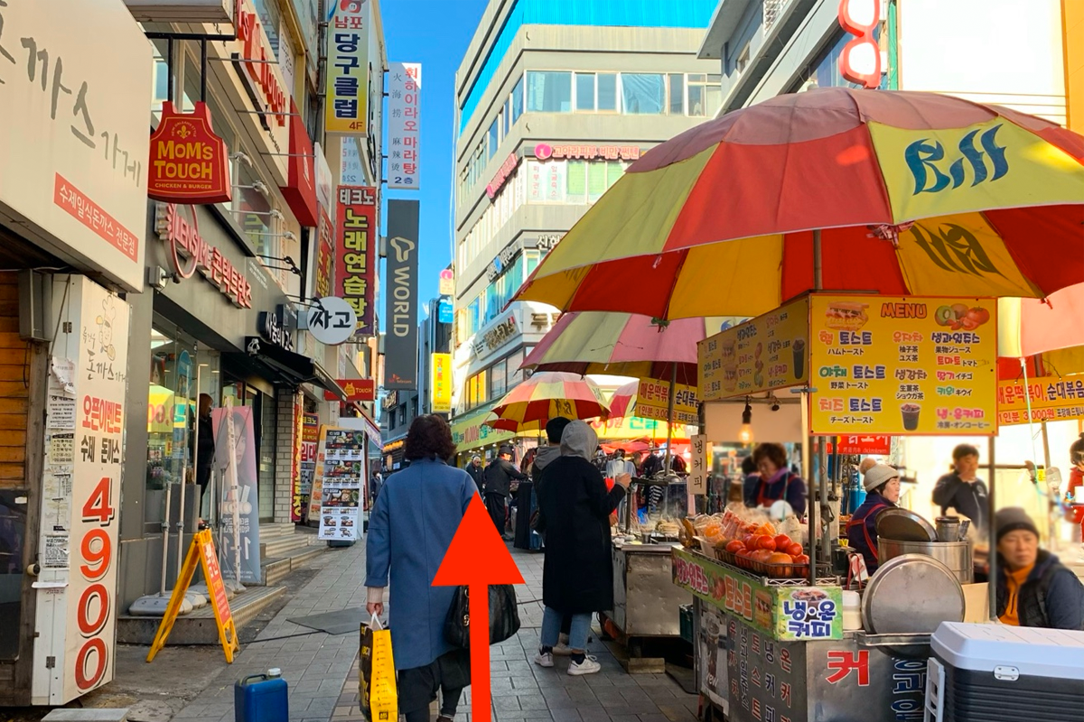 在釜山南浦洞的購物街上行走的人羣，旁邊有韓國地道的小商鋪和露天攤位。