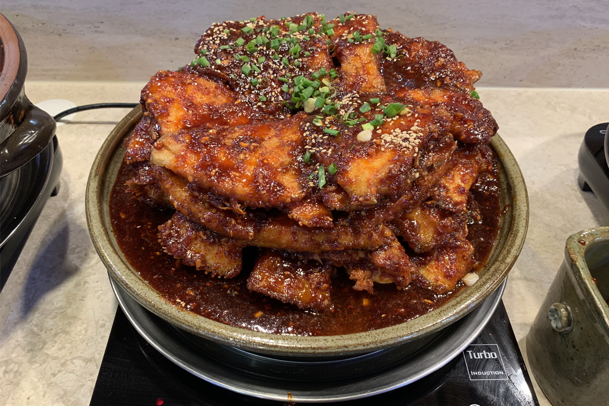 自助餐桌上的一盘香辣炖鱼，外层均匀裹着红辣椒调料和芝麻。