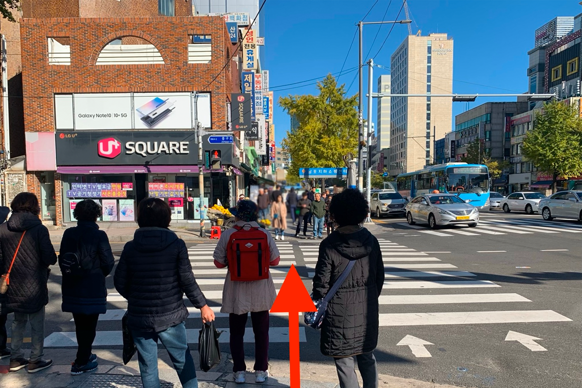 位於釜山南浦洞的U+ Square商店前的十字路口，街景充滿行人和車輛的繁忙景象。