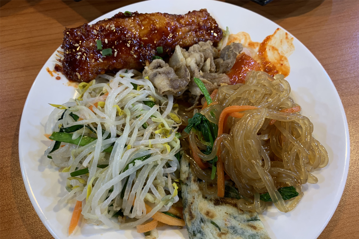 一盘色彩丰富的韩式料理，包括炒粉丝、炒肉、辣炒年糕和煎蛋饼。