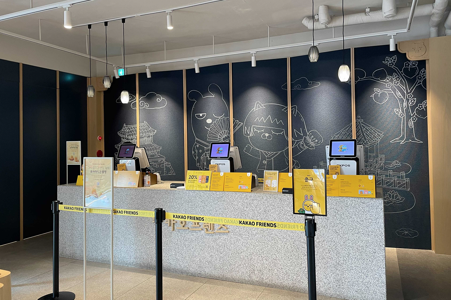 全州Kakao Friends商店的結帳櫃臺，牆上有韓服主題的圖案，描繪了韓屋及Kakao角色，看似充滿文化氛圍。