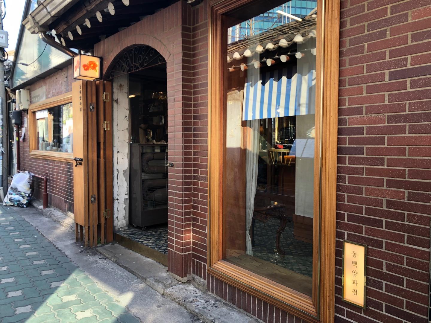 益善洞の冬柏洋菓子店の正門。レンガの外壁に白いカーテンがかかった大きな窓、そして暖かみある木製のドアが見える韓国のカフェの入り口。