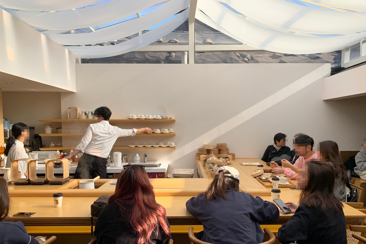 밀 토스트 하우스의 바에서 바리스타가 음료를 준비하는 장면. 손님들이 바에 앉아 있는 모습