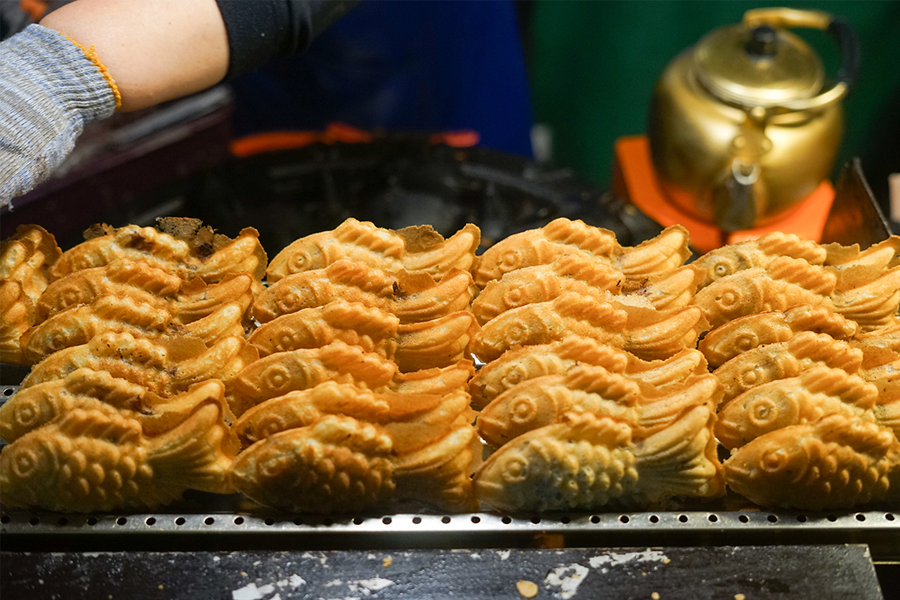 場景展示了韓國街頭販賣的鯽魚餅（붕어빵），這種含內餡的小吃向來受遊客喜愛，很多店以₩1,000的價格售3至4個。