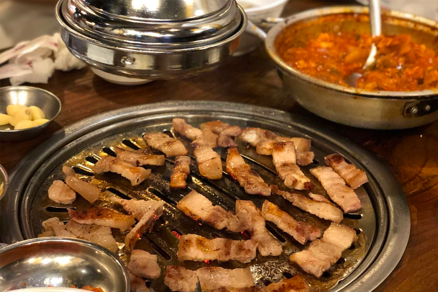 白種元旗下新村食堂的招牌烤豬五花肉,搭配肥瘦均勻的豬肉片在烤盤上散發香味。