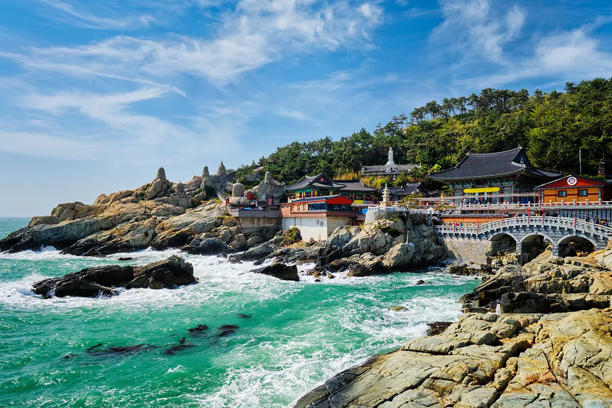 Scenic view of Haedong Yonggungsa Temple in Busan, South Korea, perched on rocky cliffs above the sparkling blue ocean.
