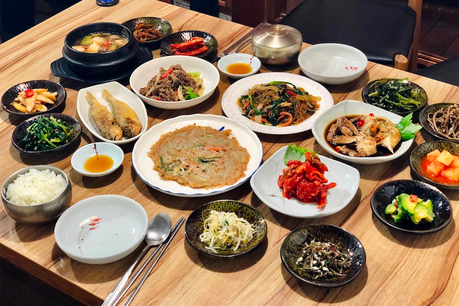 韓定食套餐的俯視圖，大量的小菜和一鍋熱氣騰騰的湯，營造出豐足的用餐體驗。