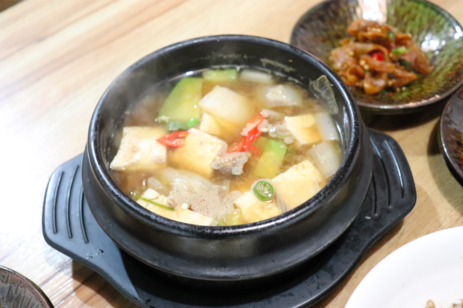 大醬湯在蒸汽中冒著泡，器皿週邊放置著韓國泡菜和小菜。