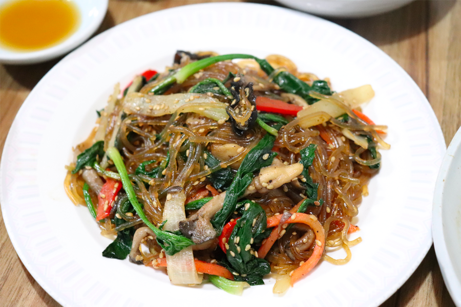 以韓式炒雜菜為主題的菜餚，上面點綴著芝麻和新鮮蔬菜。