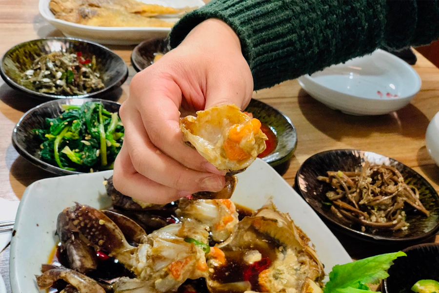 一位食客正在享用韓國醬蟹，手裡拿著一塊蟹肉，顯示出品嚐此美食的滿足感。