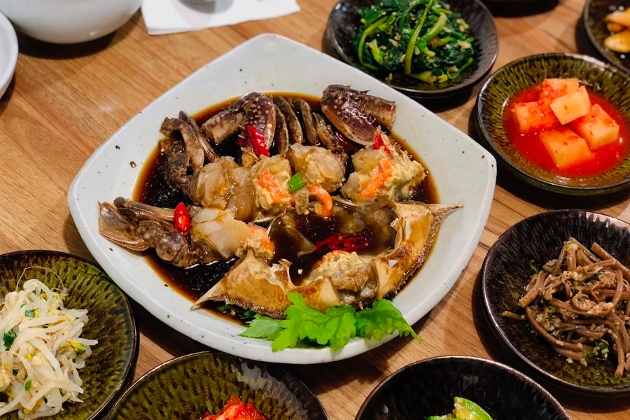 一盤擺滿小菜的韓式桌面，醬蟹為主菜，呈現傳統的韓式風味。