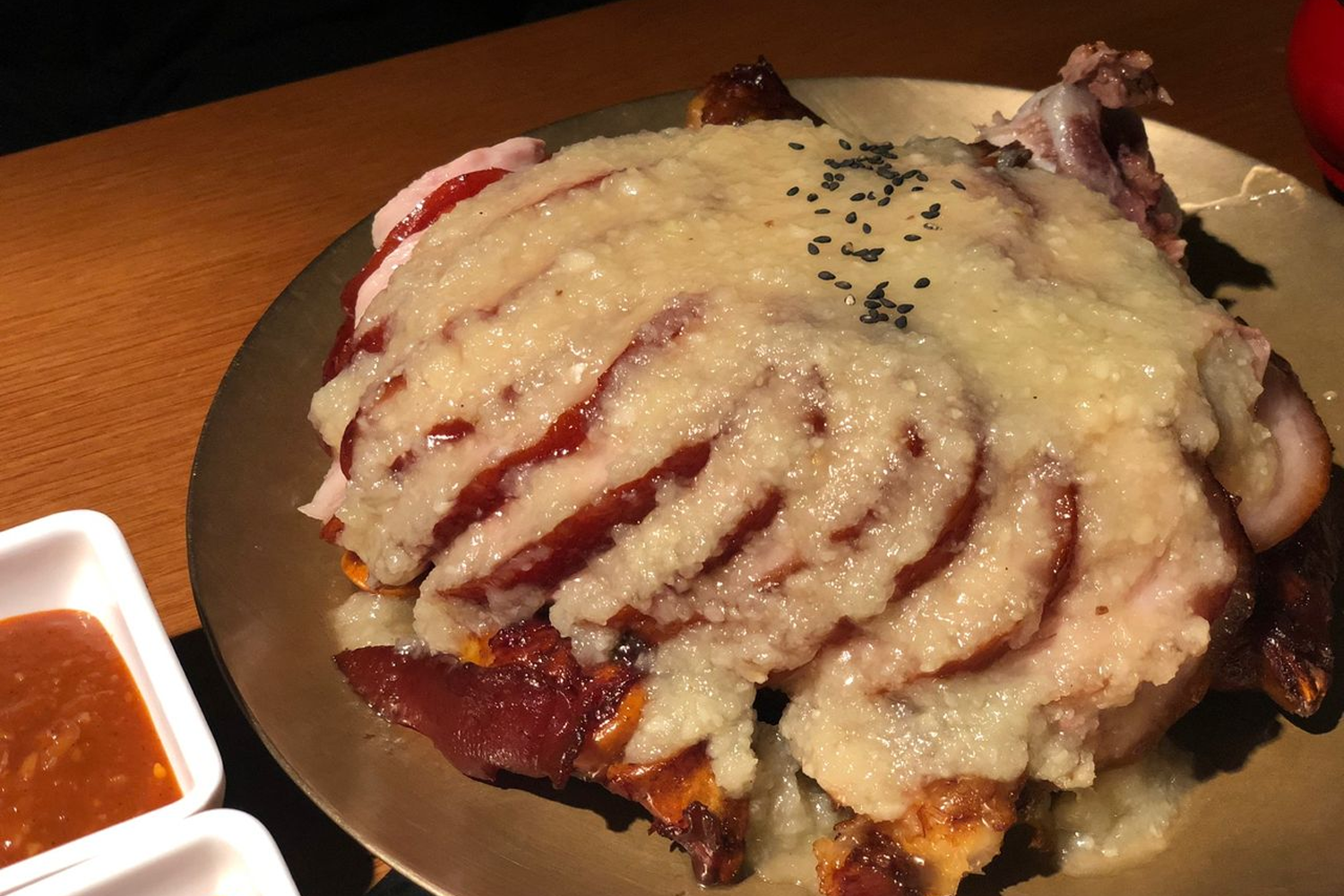 韓式豬腳上面覆蓋著厚厚芝麻醬的特寫，肉質看起來非常軟嫩，是韓國著名的熱量高菜餚之一，搭配著一碟辣醬，適合喜愛重口味的食客。