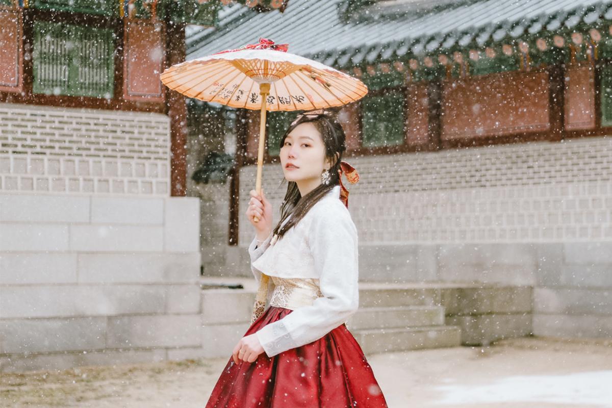 冬天在古代韓國建築前面穿著韓服並持有韓式雨傘的女子