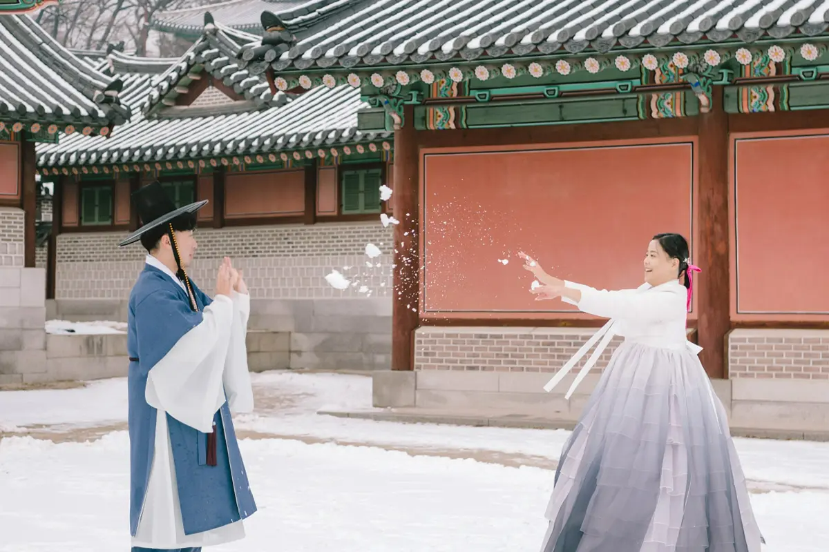 著韓服的女性在冬季韓國傳統建築前扔雪球