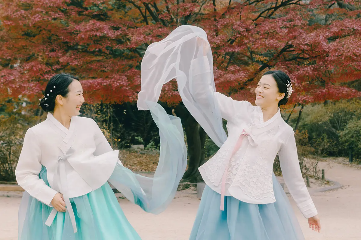 秋日落葉風景中穿著韓服的女子們愉快玩耍