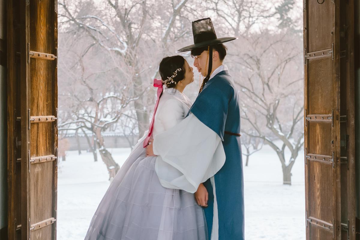 雪天在古代韓國建築前穿著韓服親密互動的兩人