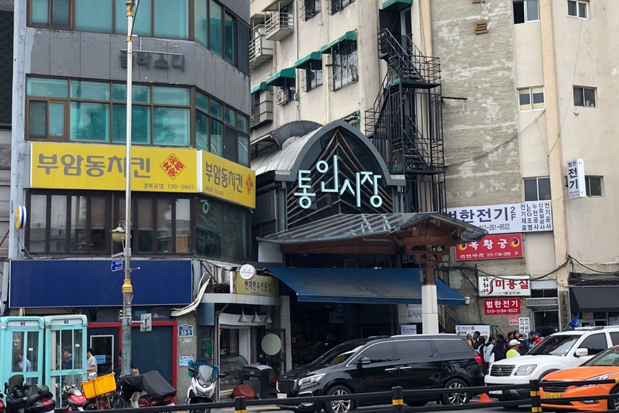 通仁市场的入口，标志性的蓝色牌匾悬挂其上，入口旁是林立的商铺和人群。