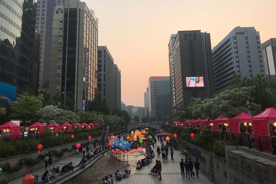 黄昏时分的清溪川，灯笼和摊贩沿着河道开放，两岸并行众多游客。