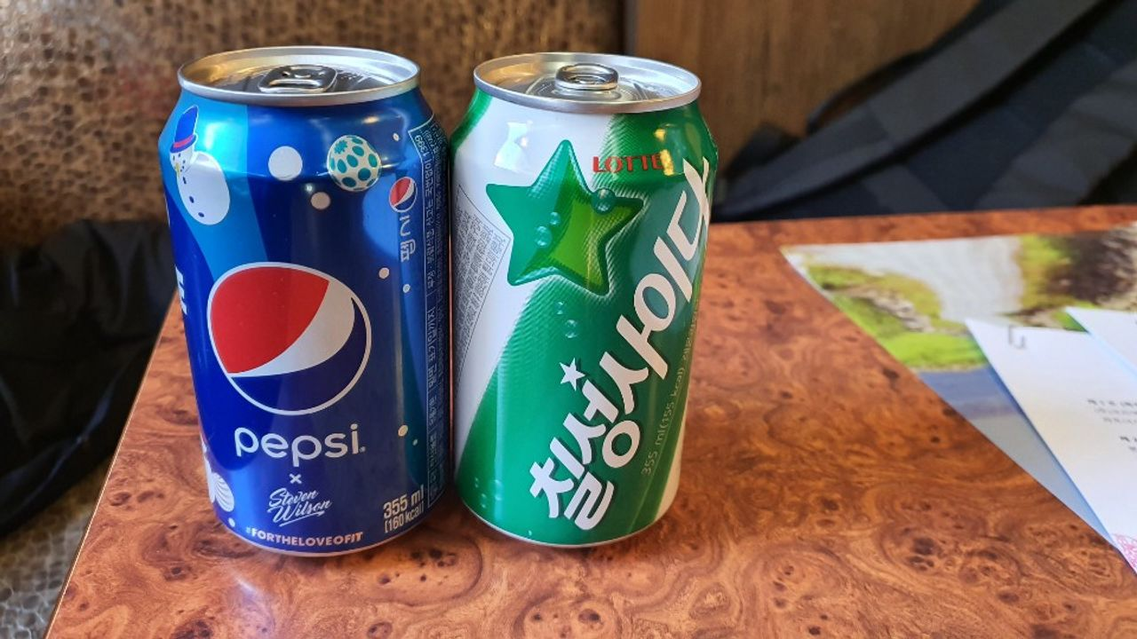 釜山のソウル元祖サムゲタン店で提供される2種類のジュース、ペプシとチルソンサイダーの缶がテーブルに置かれている様子。韓国旅行中にこのお店を訪れる際に使えるお得なクーポンプランの一部として紹介されている。