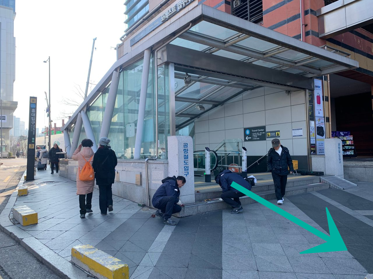 弘大地鐵站3號出口的外觀，入口前有數位訪客，背景是一座現代綠色建築。