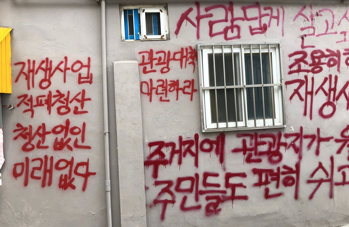 梨花洞壁畫村的一面牆上，有紅色噴漆字樣，反映了當地居民對觀光客入侵的抵制情緒，這裡曾經是著名的藝術景點。