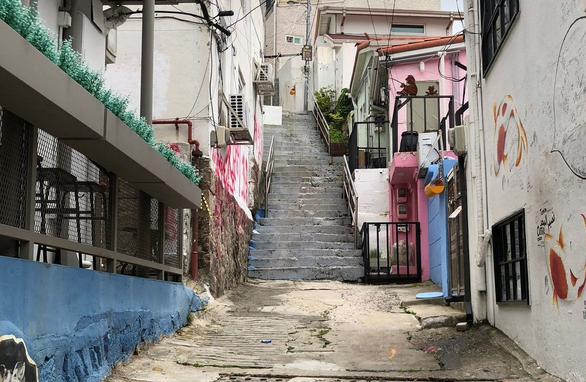 梨花洞壁畫村的一條狹窄小巷，樓梯兩邊是彩色裝飾的牆壁，這裡曾是首爾熱門的藝術景點，但受當地居民的抵制而開始消逝。