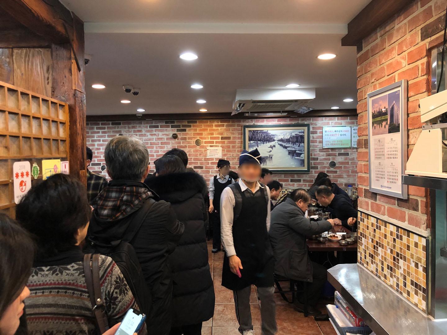 鐘閣駅近くの武橋洞プゴグッチッで並んでいる様子を撮影した画像。店内はレンガ壁に囲まれており、多くの客が待っている様子が見られます。